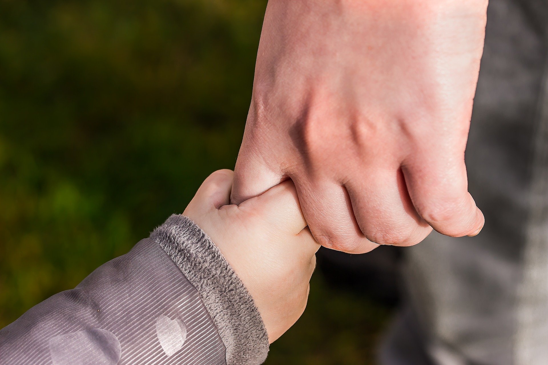 A child's hand grasping the finger of an adult