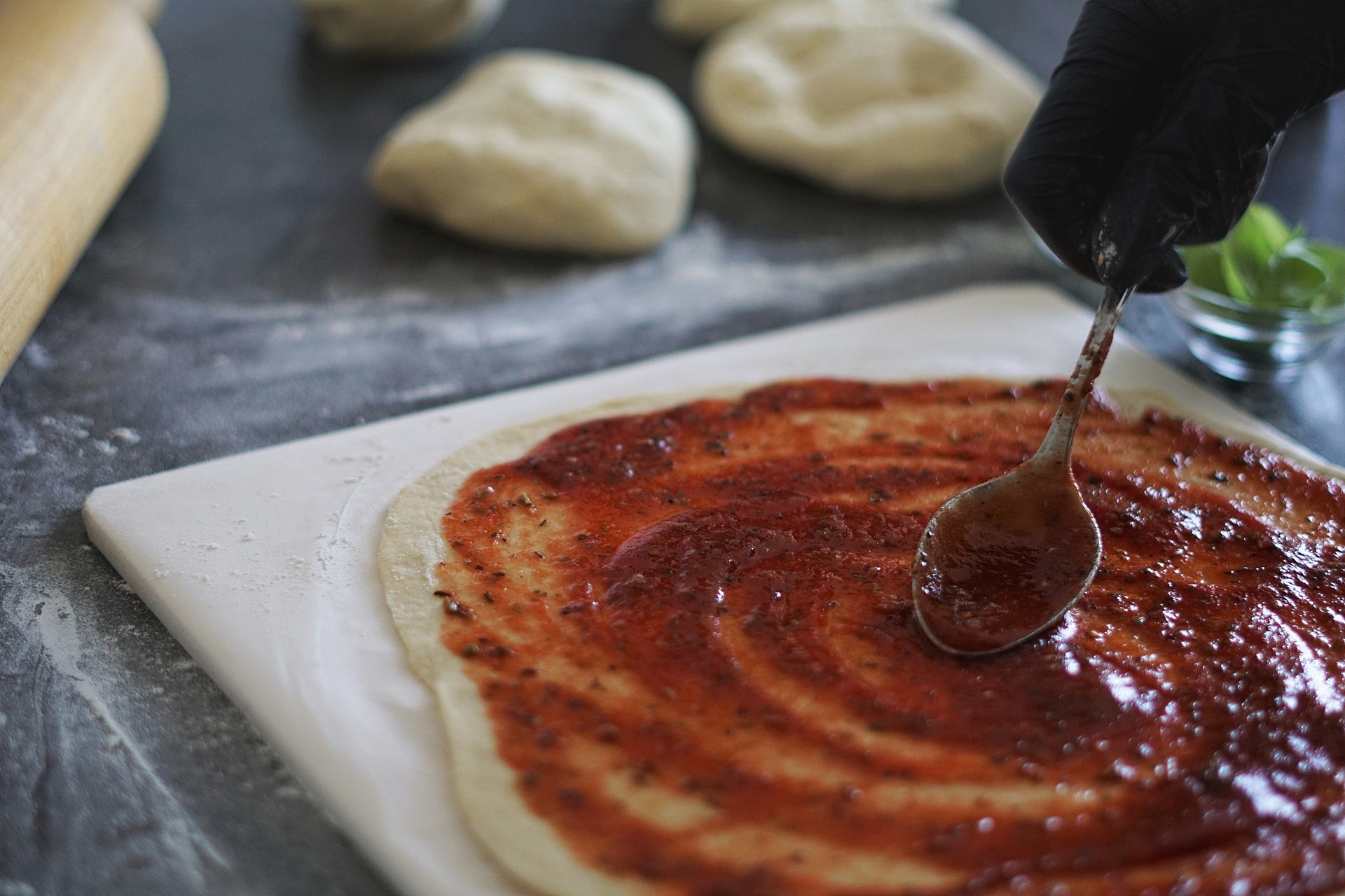 Spreading sauce on pizza dough with a spoon