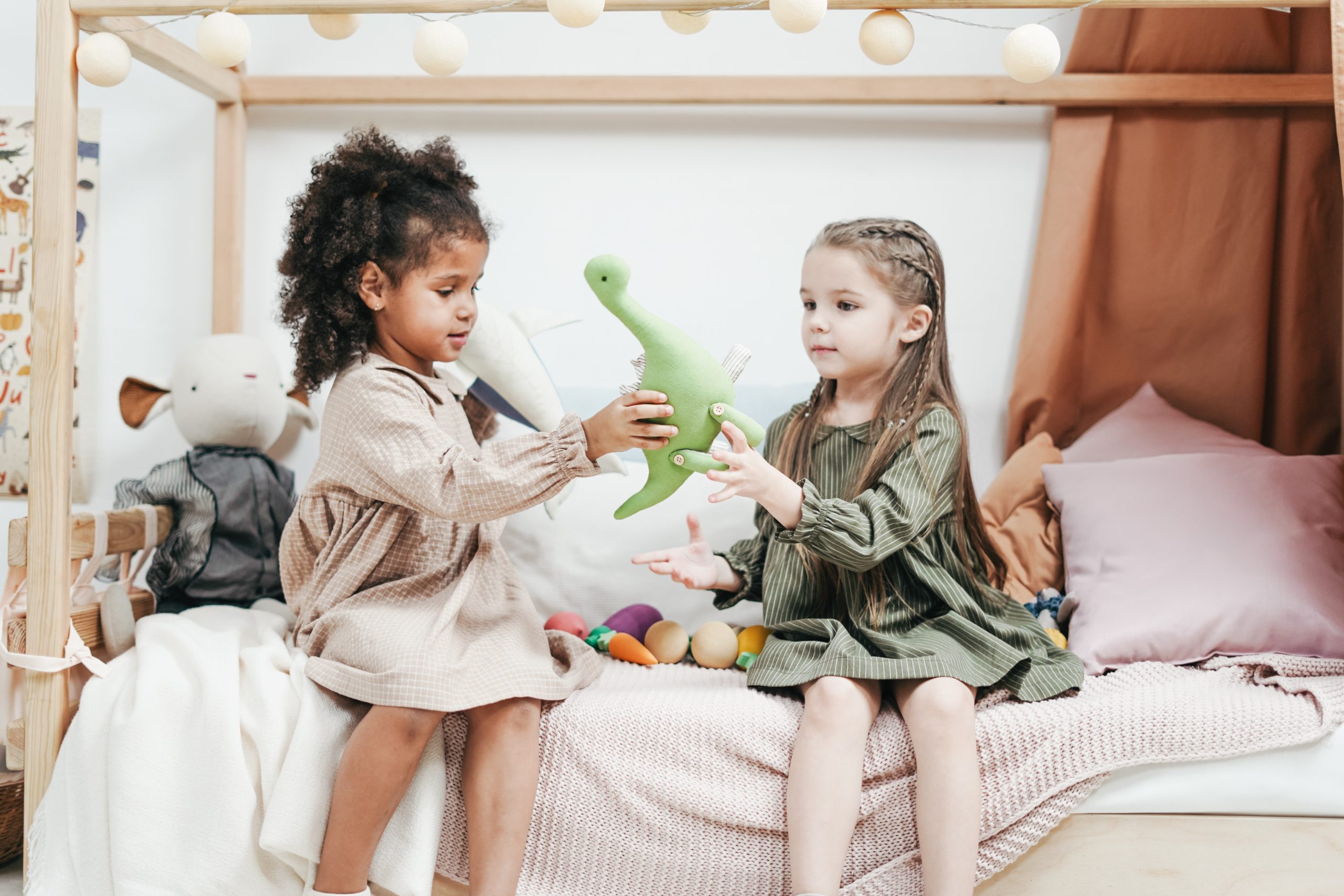 Two children holding a green dinosaur toy