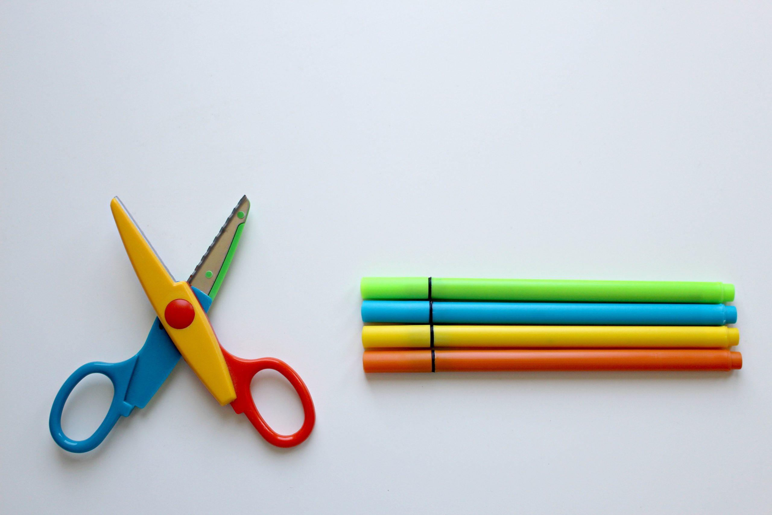 A colorful pair of scissors next to a set of colored pens